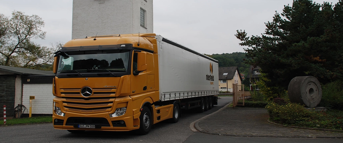 Orangefarbener LKW mit einem weißen Auflieger mit dem Aufdruck des Logos